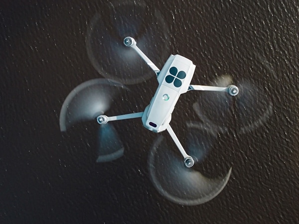 A white drone-rtk with four propellers flies above dark water, creating blurred circular patterns with its spinning blades. The drone is viewed from above.