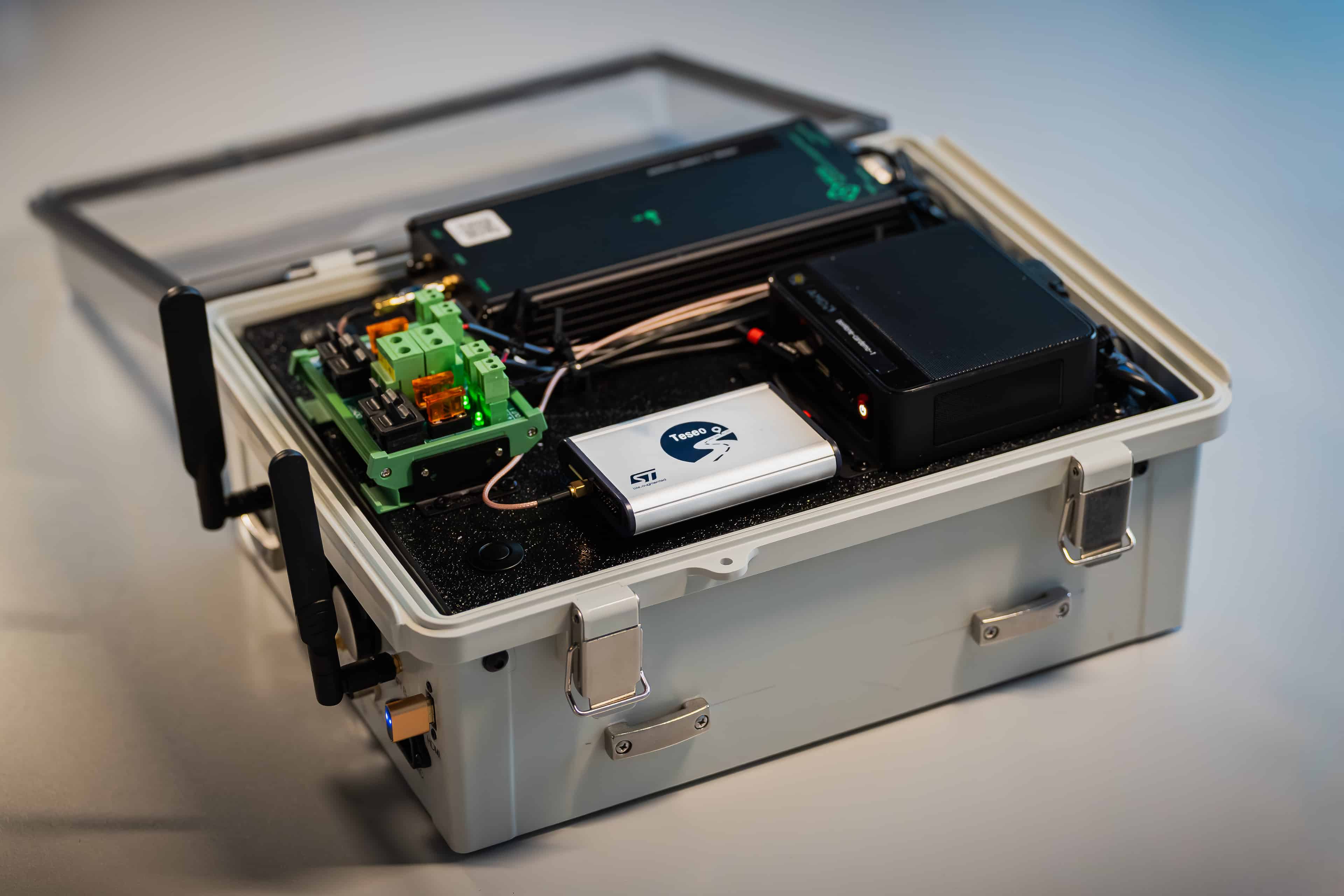 A portable equipment case, showcased at CES, contains electronic components, circuit boards, cables, and two antennas, with a labeled white device inside. The case is open on a white surface.