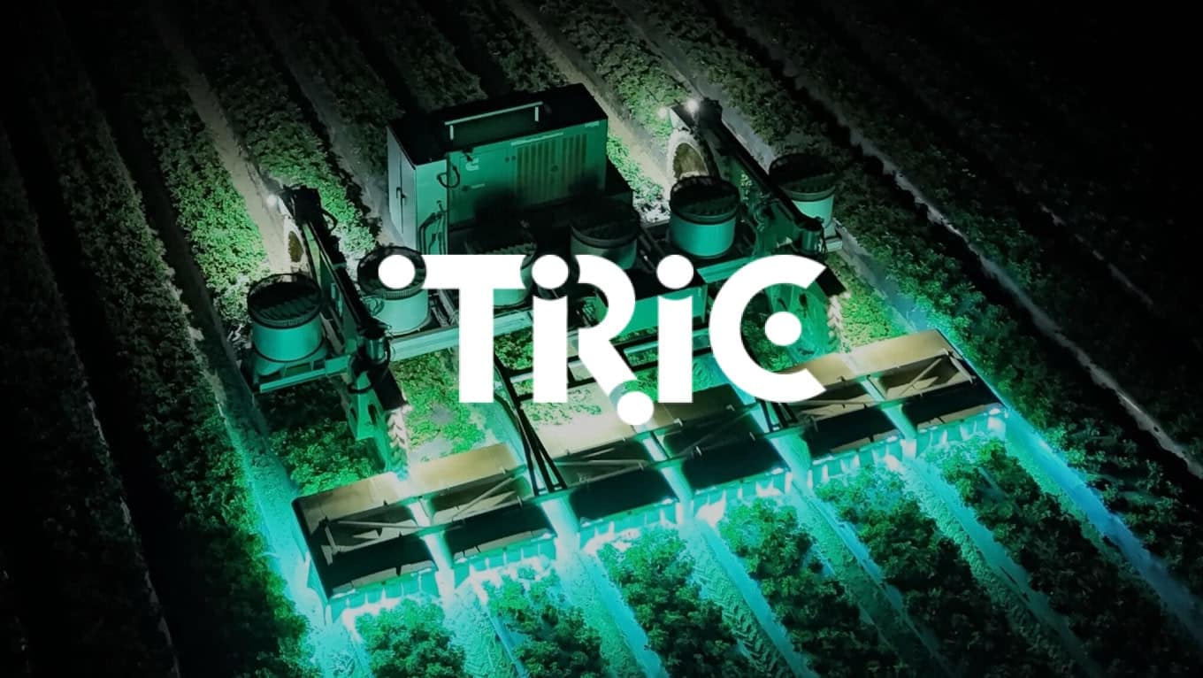 Aerial view of a large farming machine with bright teal lights illuminating crop rows at night, with the word “TRIC” in bold, stylized white lettering overlaid on the image.