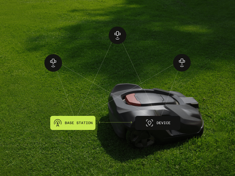 A black robotic lawn mower on grass, with digital icons above it indicating connectivity to a base station and multiple sensors or devices.
