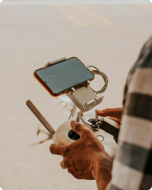A person holding a drone remote controller with a smartphone attached, focusing on their hands and the device, ready for flight outdoors.