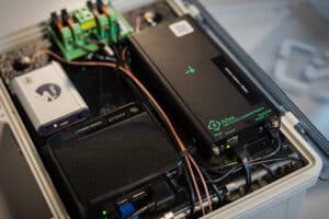 A close-up of an electronics enclosure with various devices, including a modem, Atlas environmental sensor, control panel, and several cables neatly connected to terminals—ideal for monitoring positioning engine location within advanced systems.