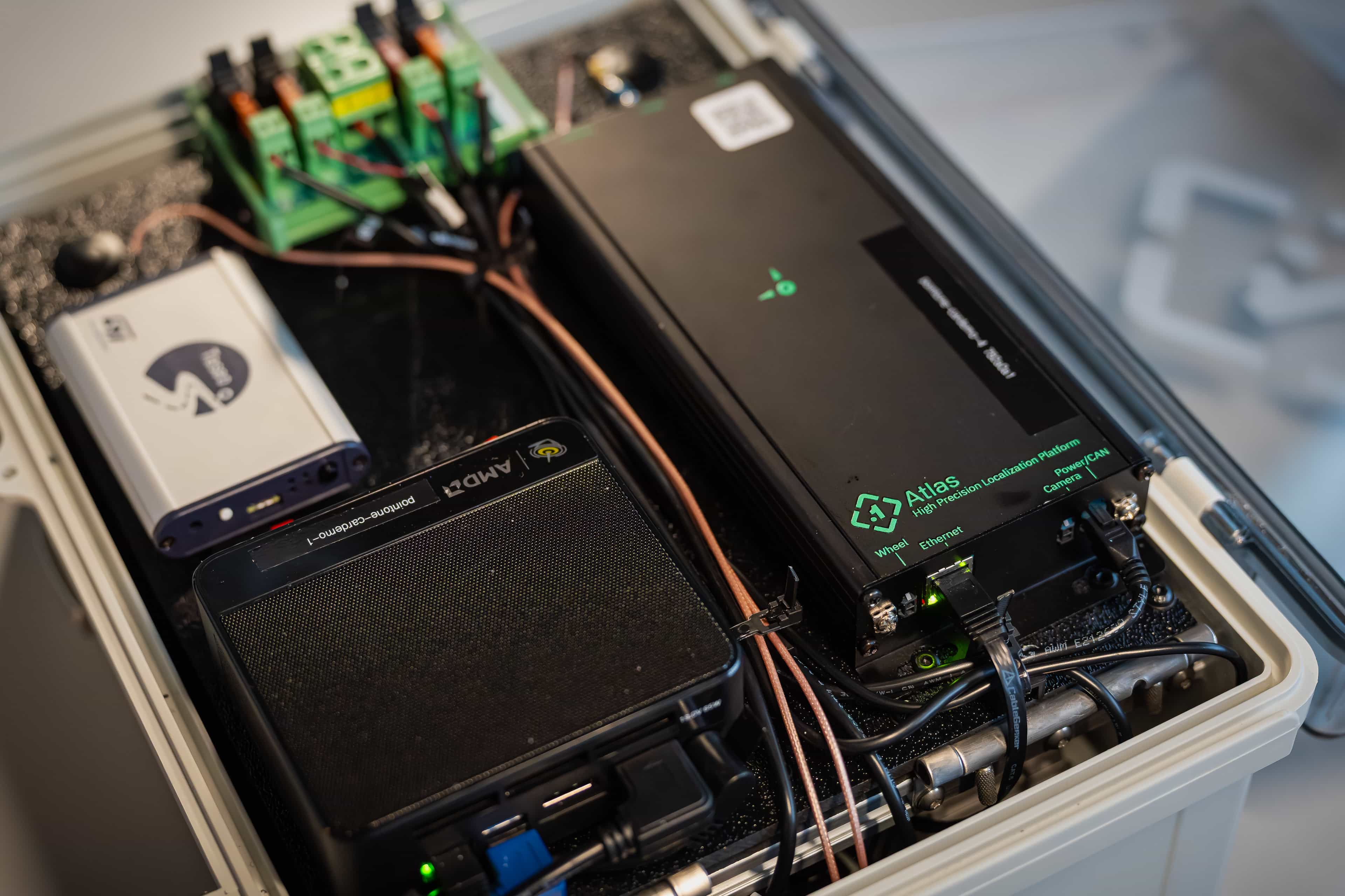 A close-up of an electronics enclosure with various devices, including a modem, Atlas environmental sensor, control panel, and several cables neatly connected to terminals—ideal for monitoring positioning engine location within advanced systems.